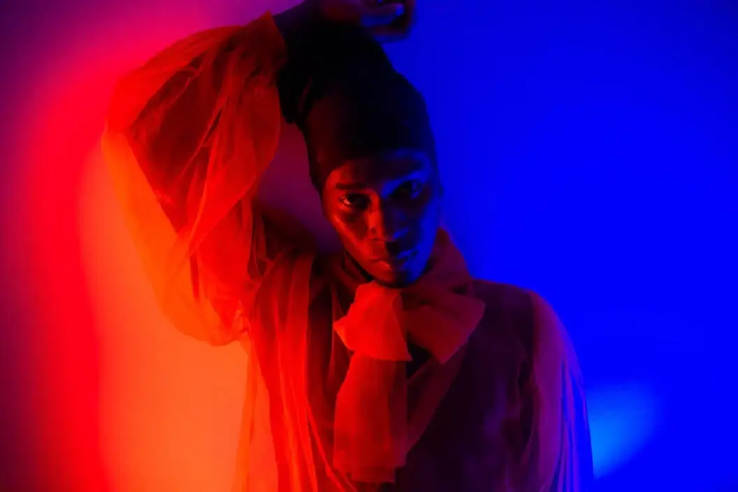 Person in a sheer orange blouse under dramatic red and blue lighting